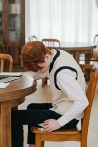 A woman holds her forehead with one hand while sitting at a kitchen table, looking tired and overwhelmed.