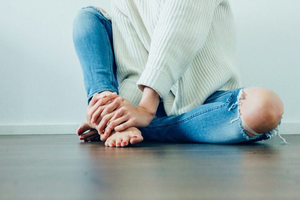 Person gently checking a tingling foot while seated, with a hand and bare foot clearly visible.